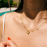 Close-up of a person wearing a gold necklace with a flower pendant, outdoors.