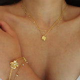 Close-up of a person wearing a gold necklace and bracelet with floral designs.