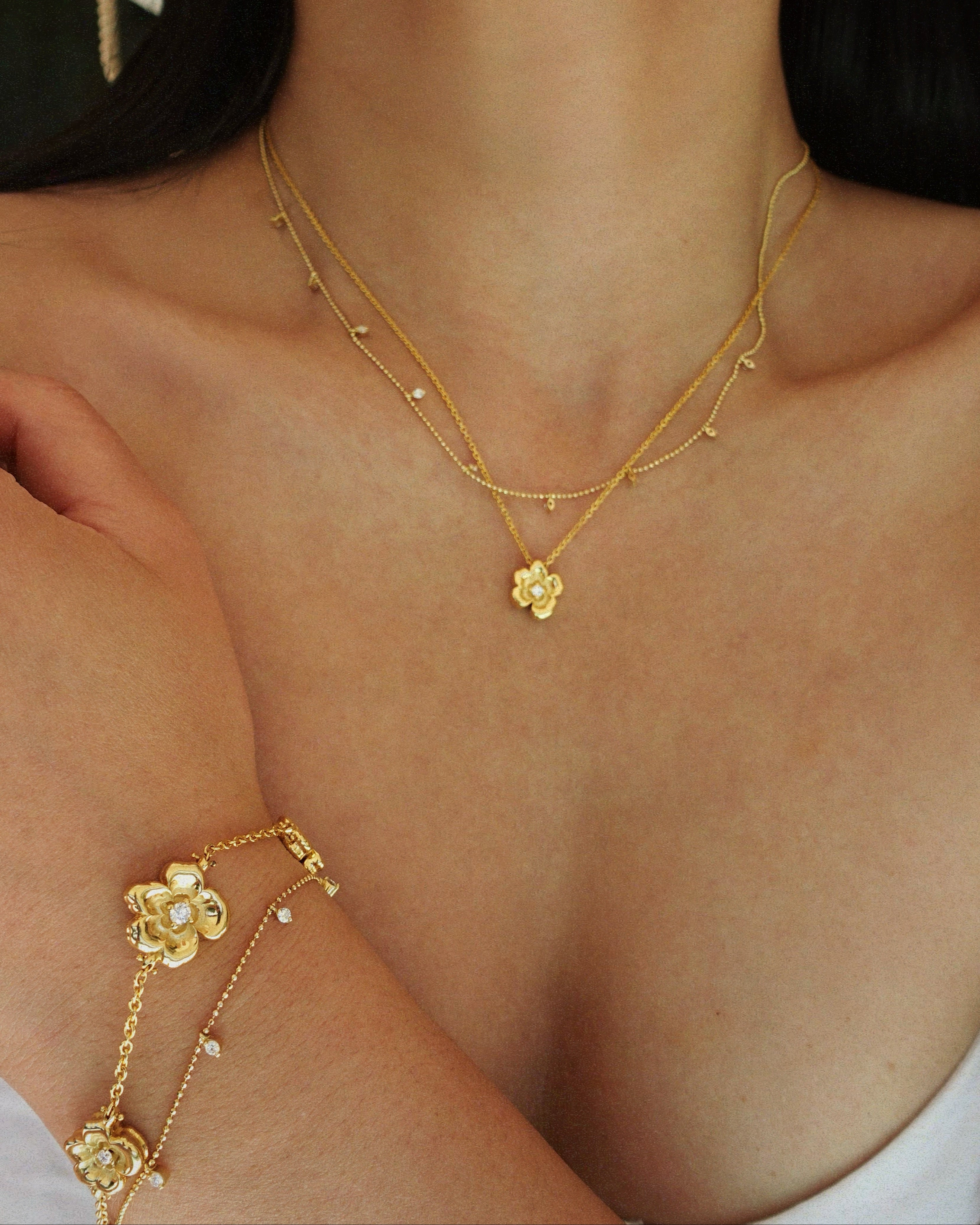 Close-up of a person wearing a gold necklace and bracelet with floral designs.