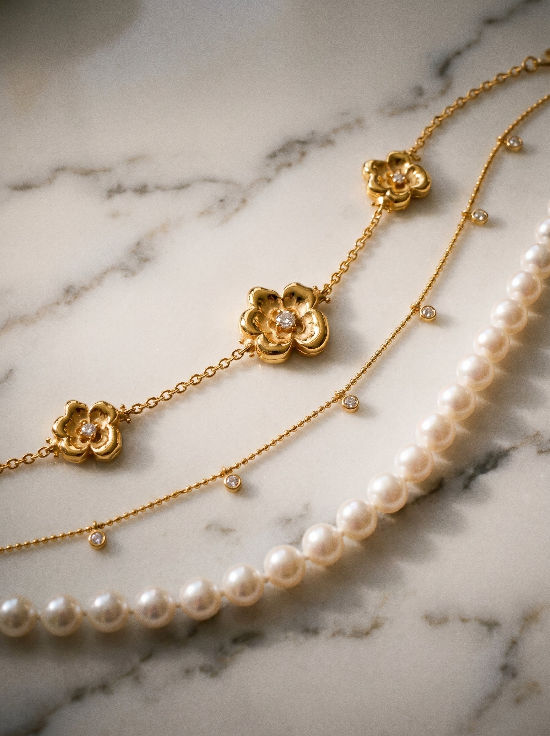 Gold necklace with floral pendants and pearl necklace on a marble surface