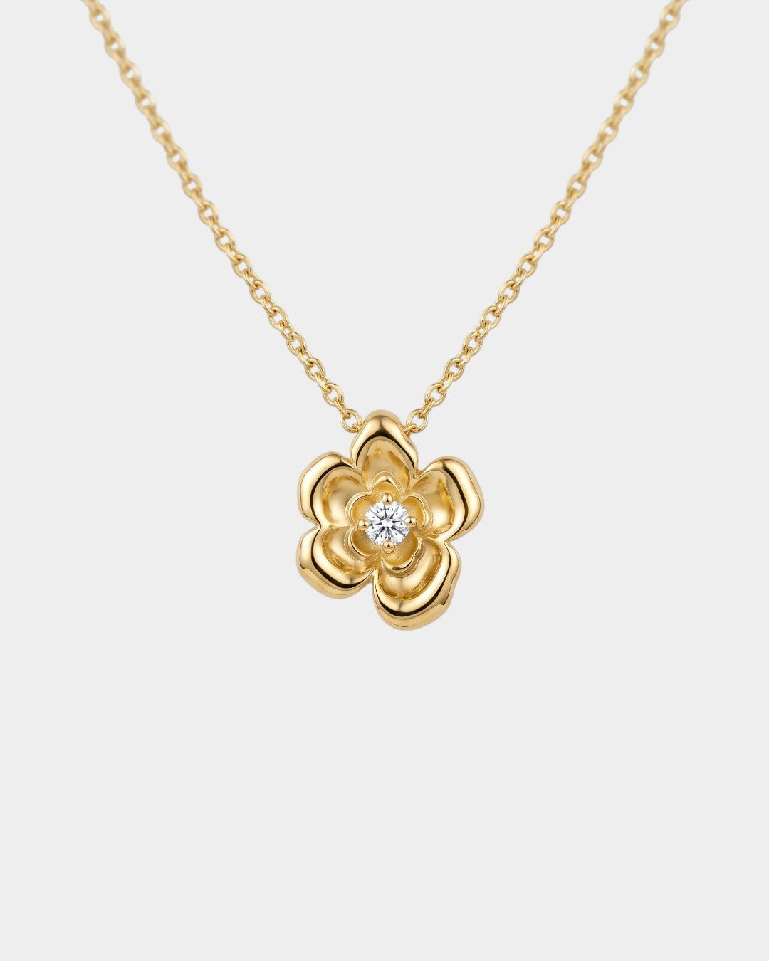 Gold flower-shaped pendant necklace with a diamond on a light gray background