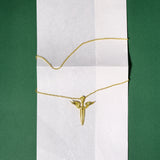 Gold necklace with a sword-shaped pendant on a white card against a green background