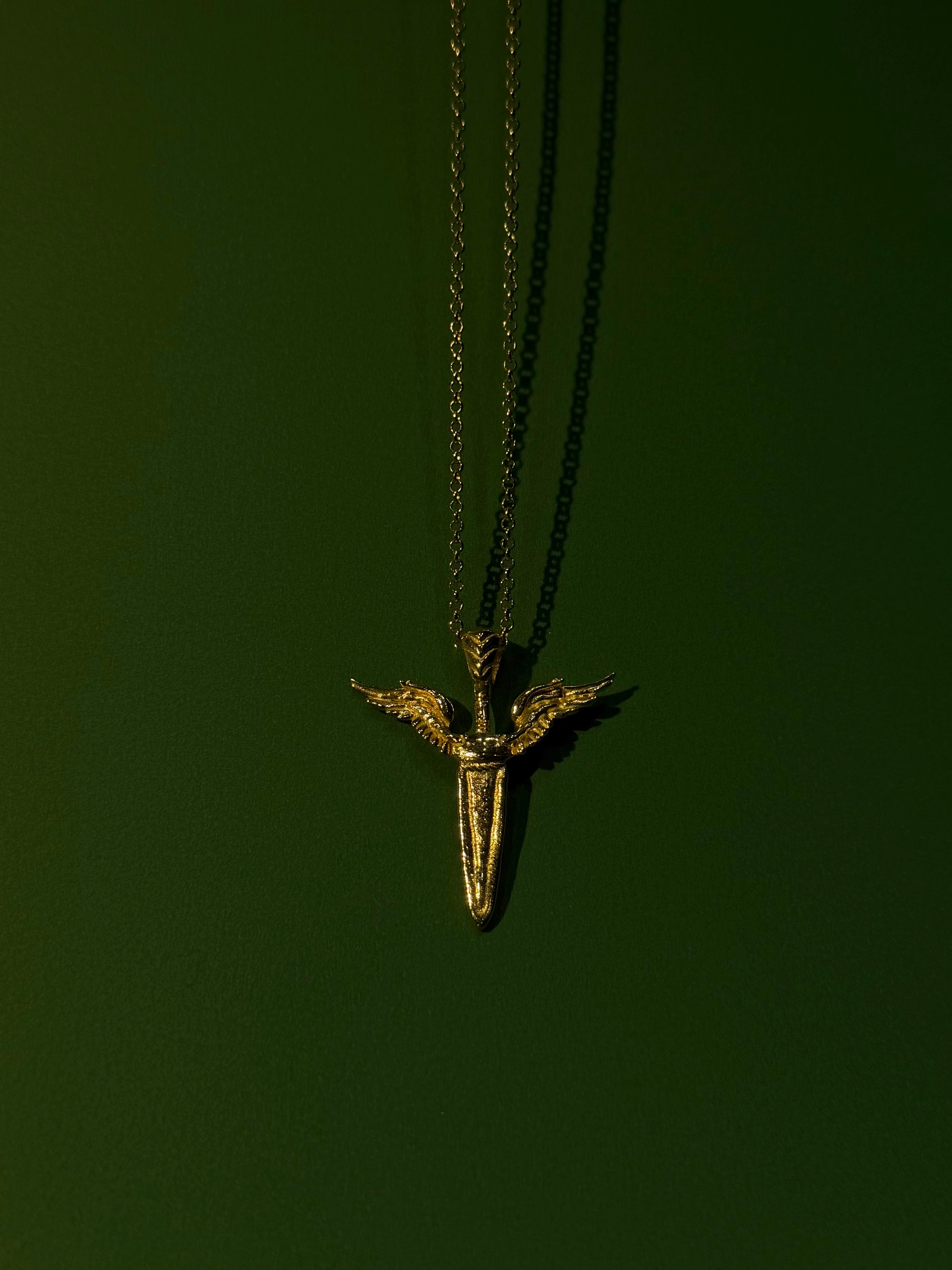 Gold necklace with a shark tooth pendant on a dark green background