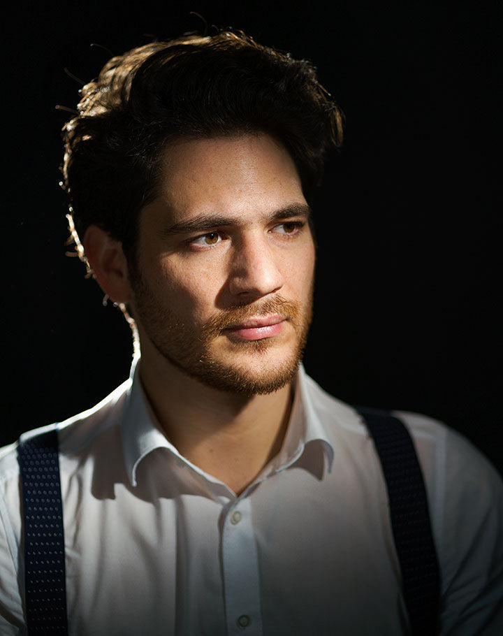 Man wearing a white shirt and suspenders against a dark background