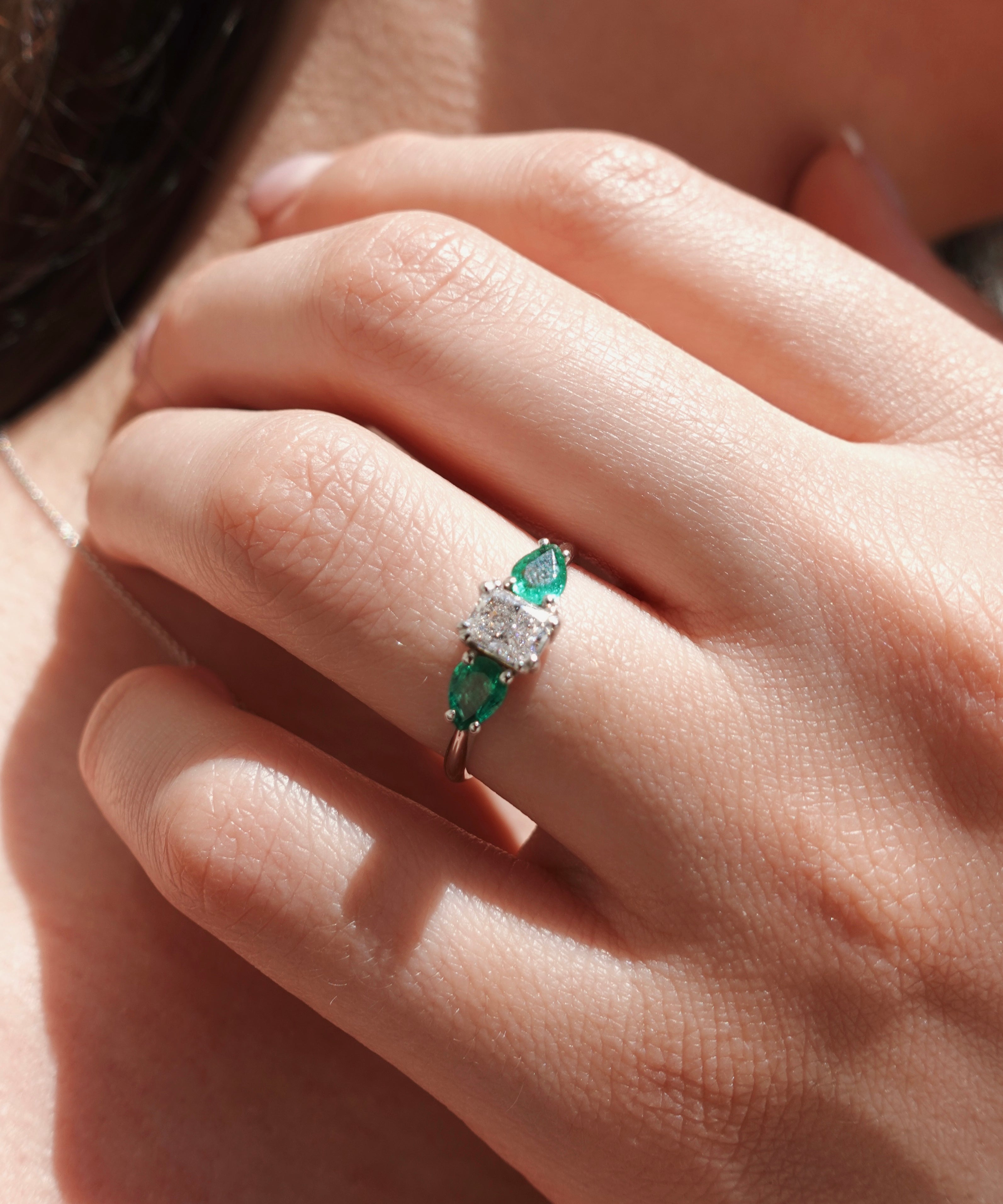 Close-up of a hand wearing an emerald and diamond ring.