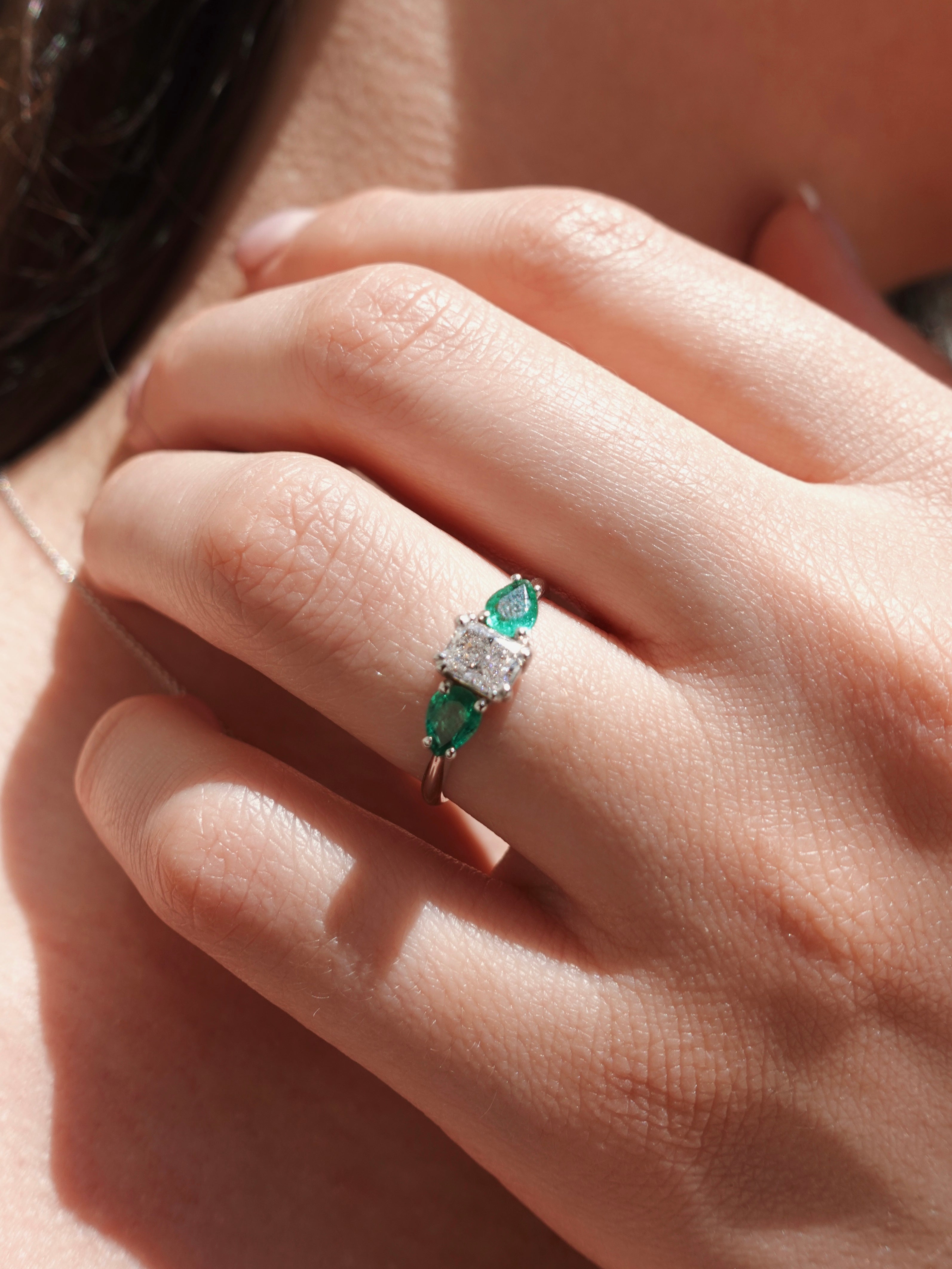 Close-up of a hand wearing an emerald and diamond ring.