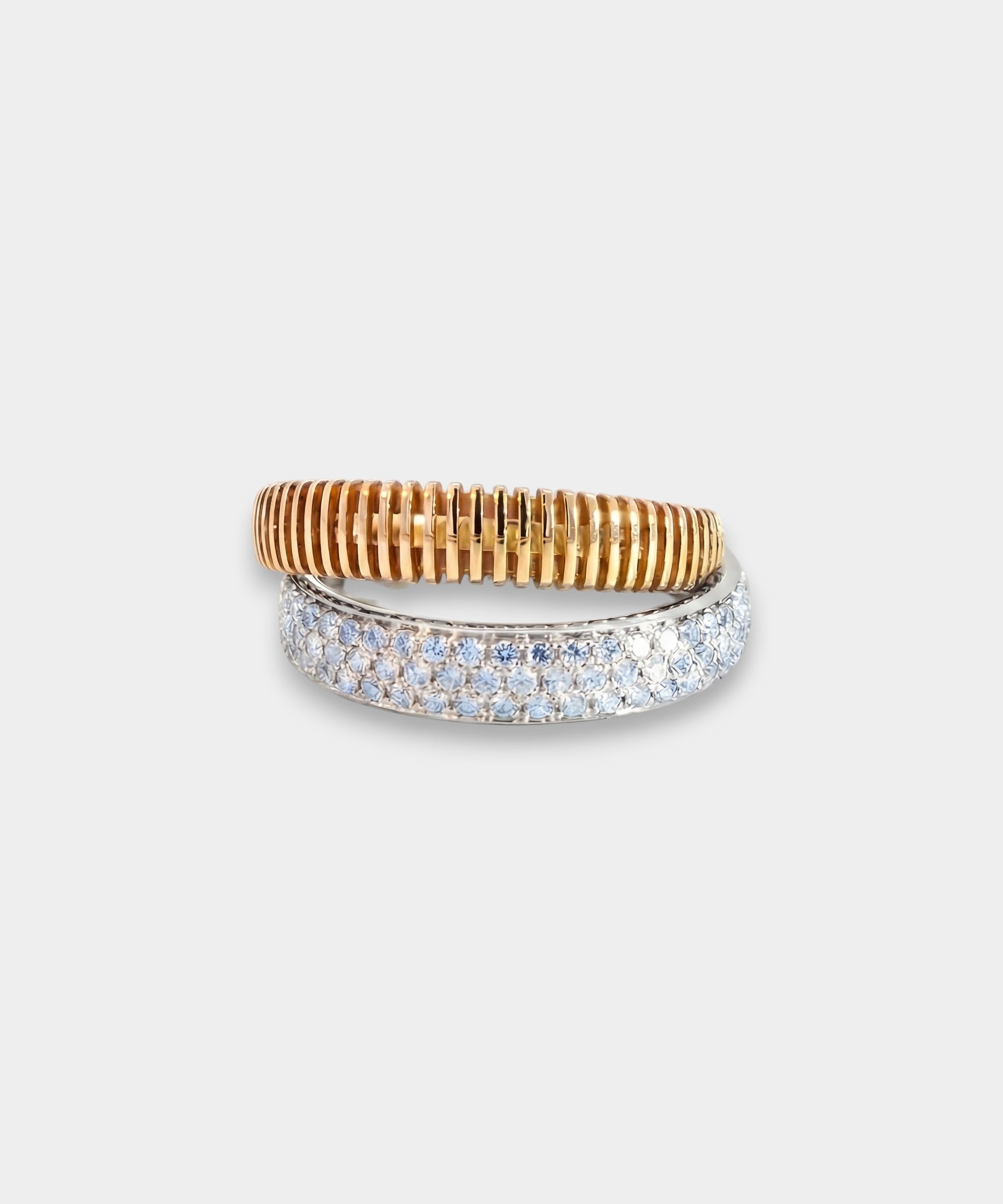 Two rings as one, one gold and one white gold with diamonds, on a light gray background