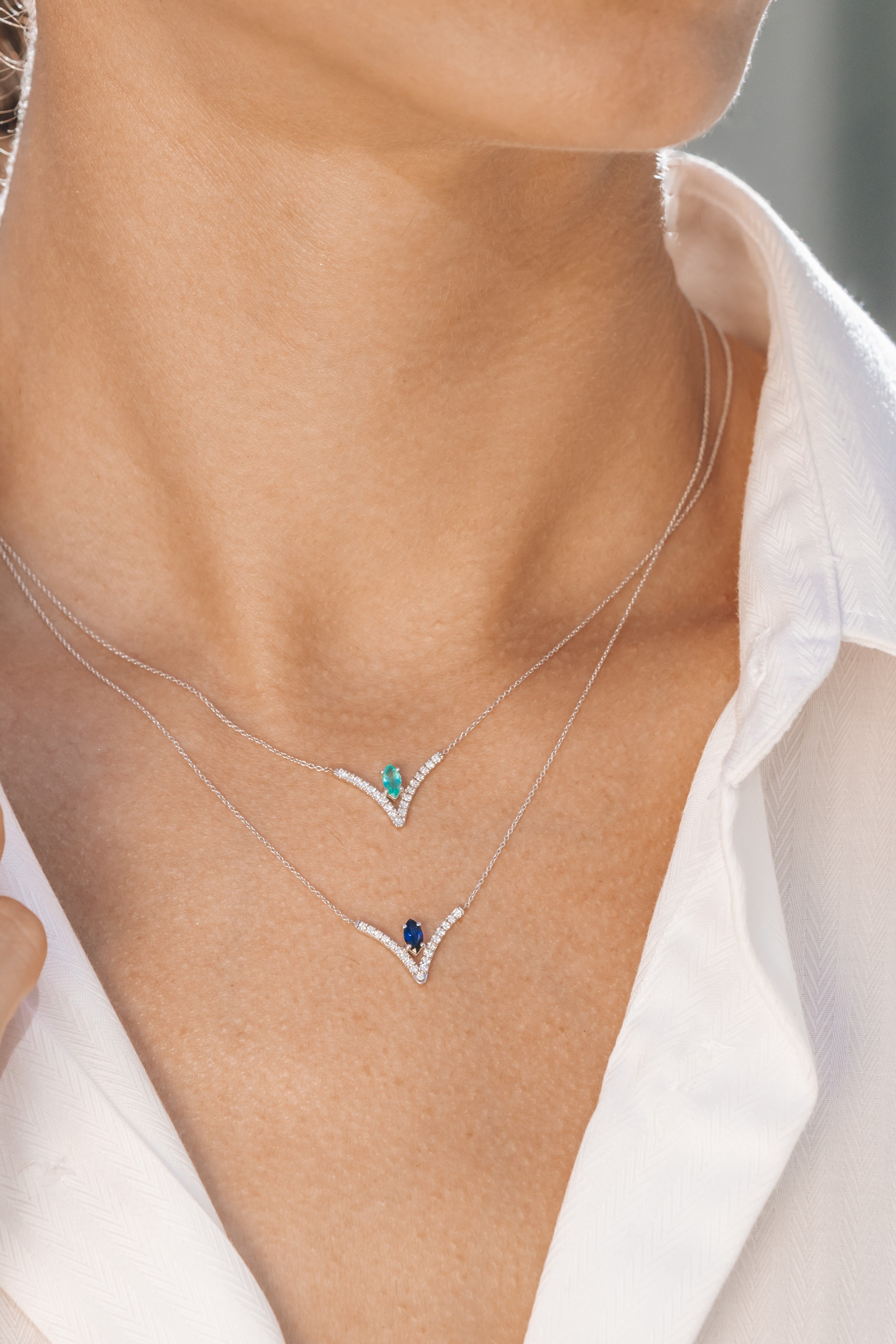 Necklace with blue and green gemstones worn by a person in a white shirt.