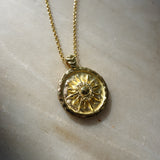Gold necklace with a circular pendant on a marble surface