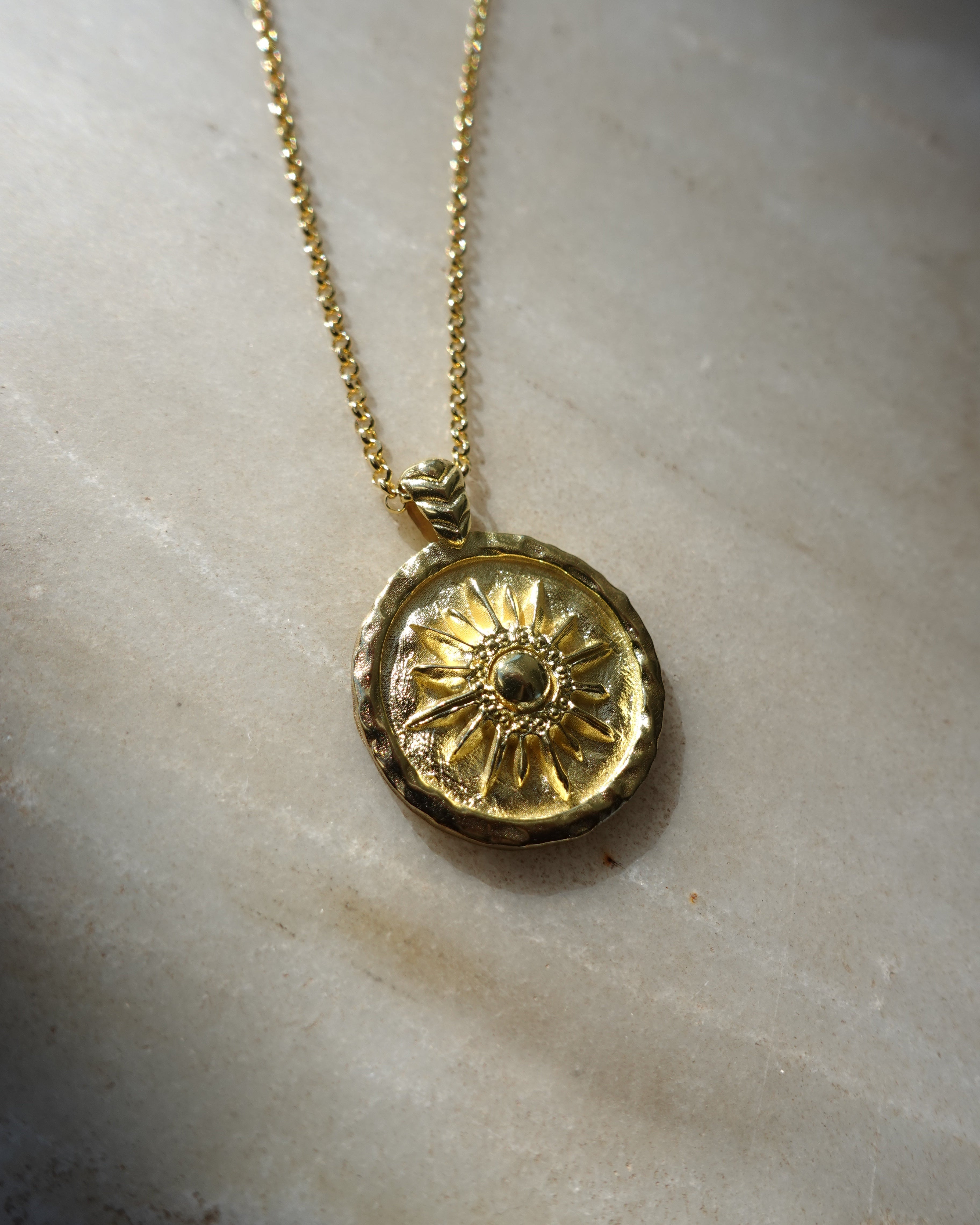 Gold necklace with a circular pendant on a marble surface