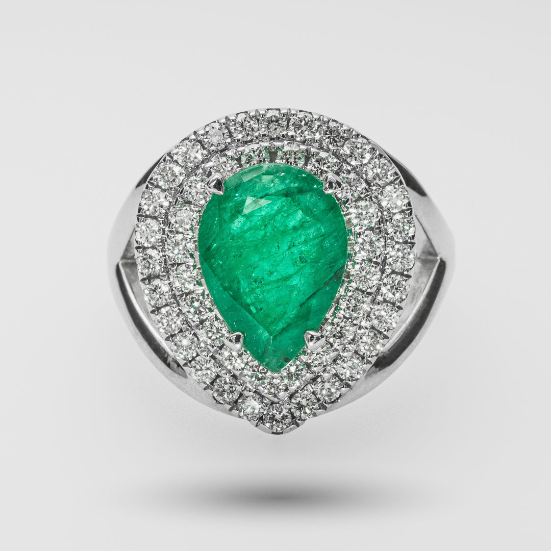 Ring with a green gemstone and diamond-studded halo on a light gray background