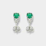 Pair of white-gold earrings with emeralds on a light gray background