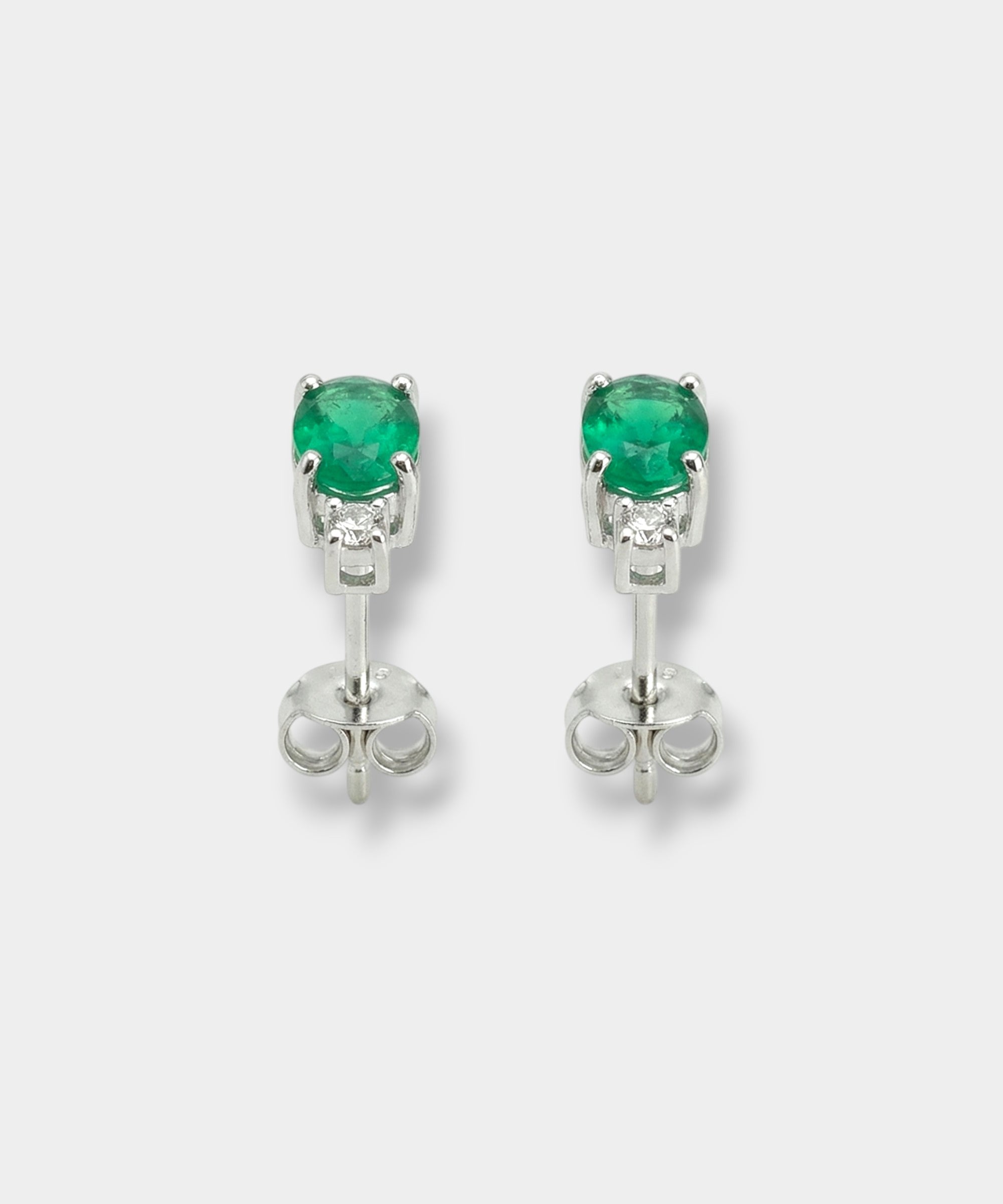 Pair of white-gold earrings with emeralds on a light gray background