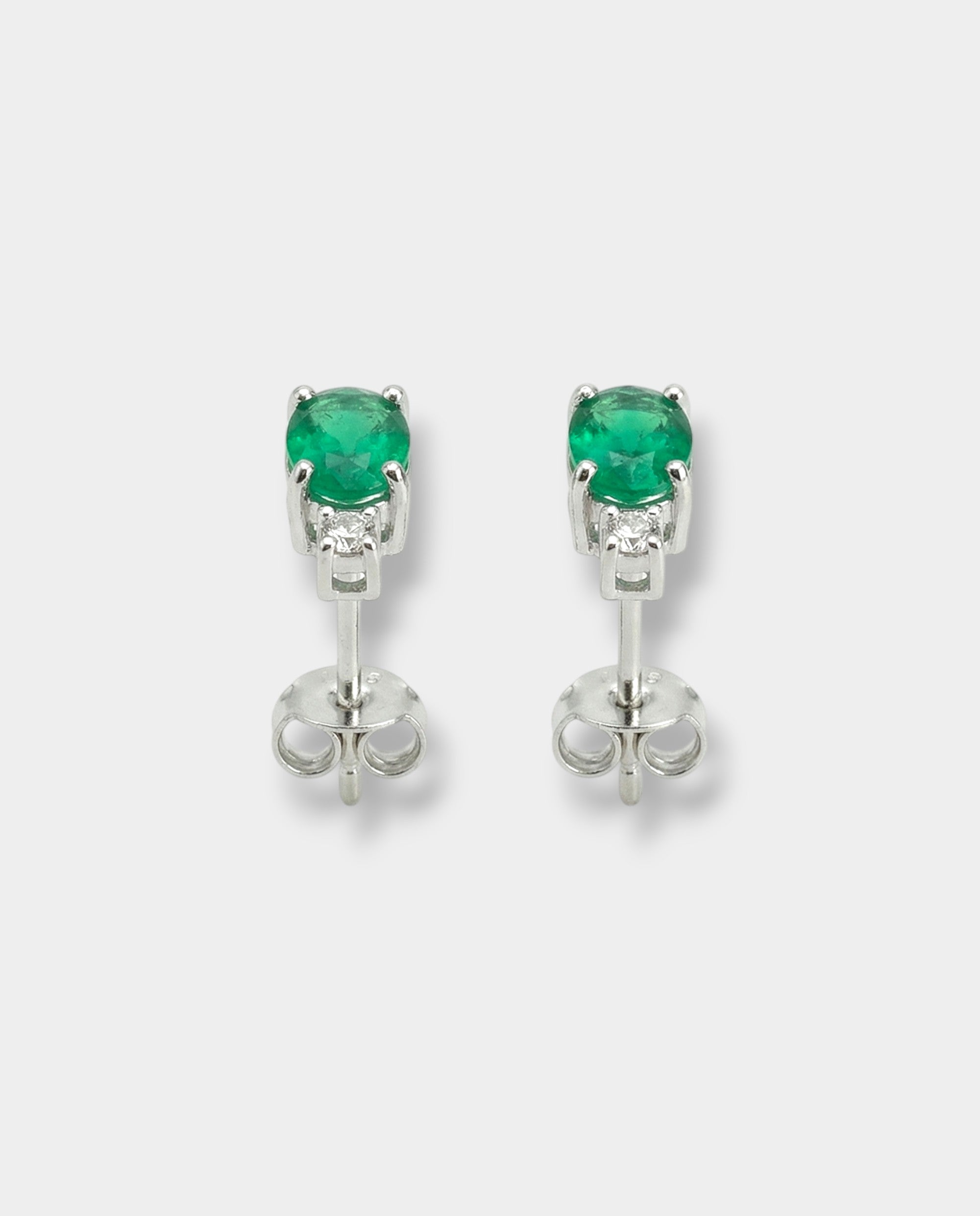 Pair of white-gold earrings with emeralds on a light gray background