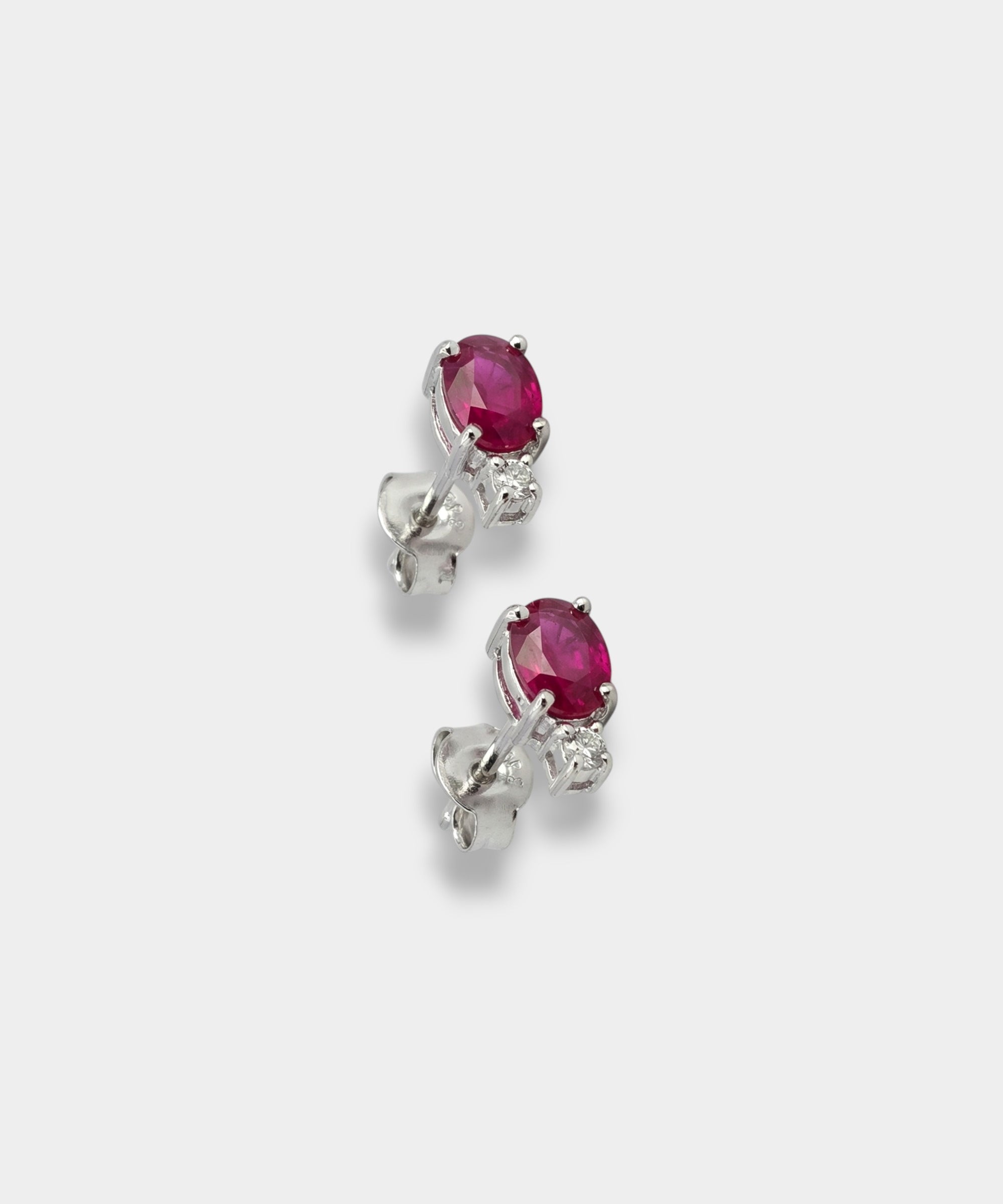 Pair of white-gold earrings with rubies on a light gray background