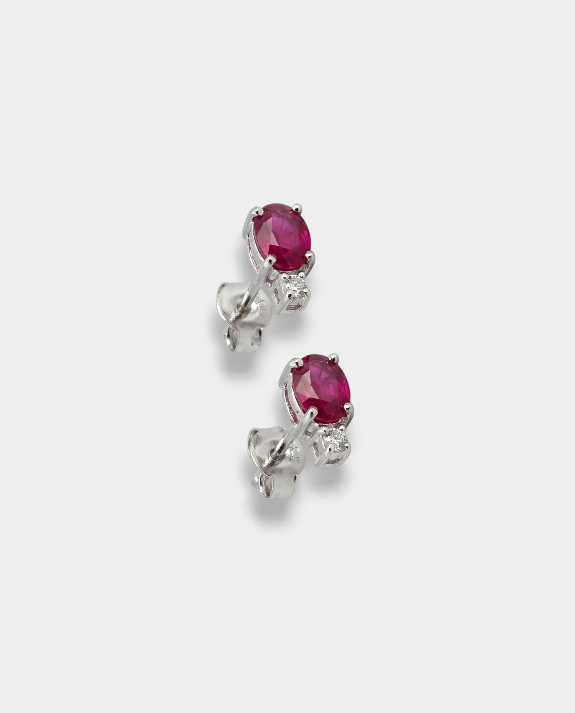 Pair of white-gold earrings with rubies on a light gray background