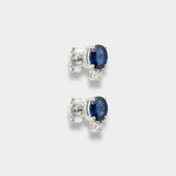 Pair of white-gold earrings with blue sapphires on a light gray background