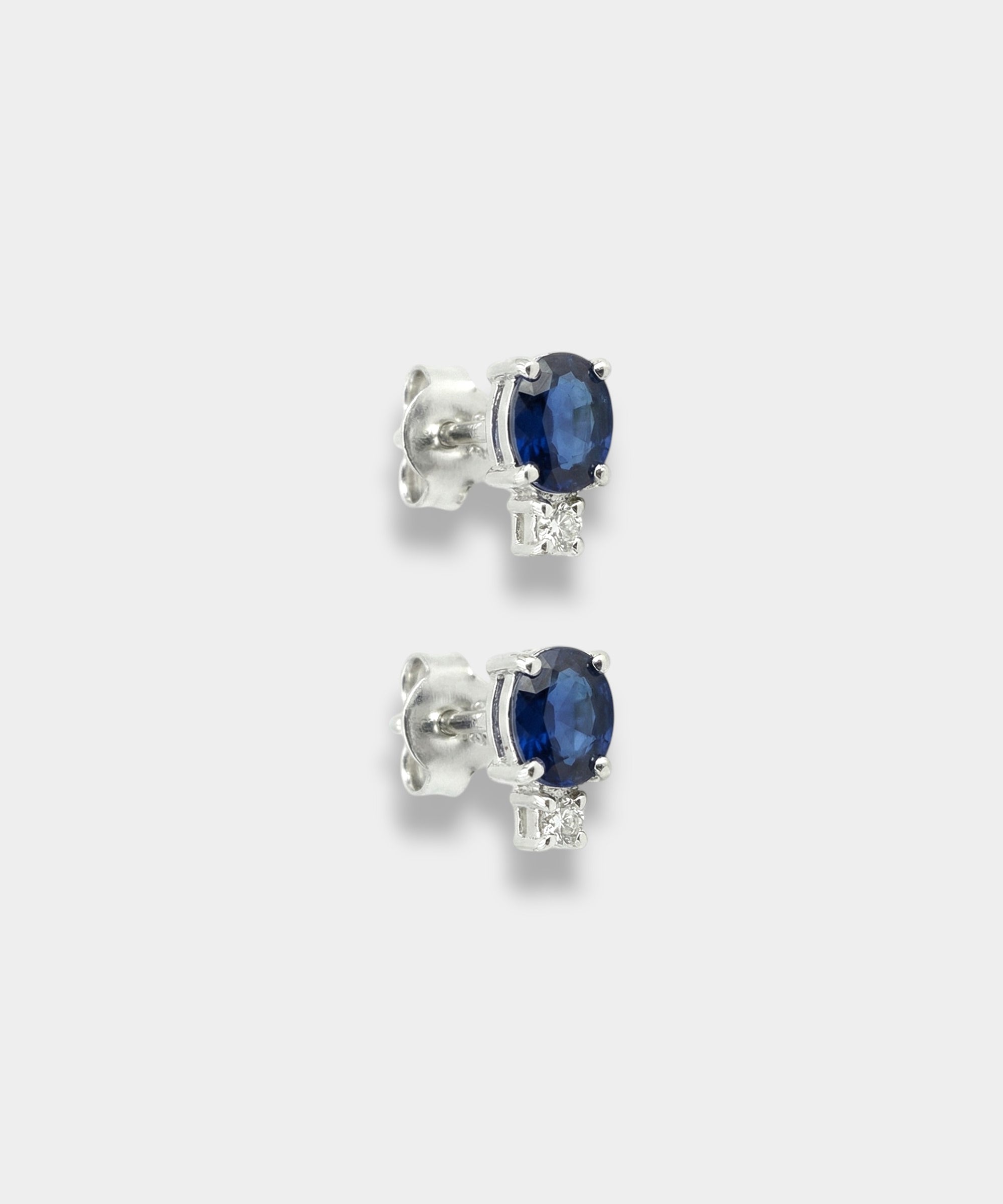 Pair of white-gold earrings with blue sapphires on a light gray background