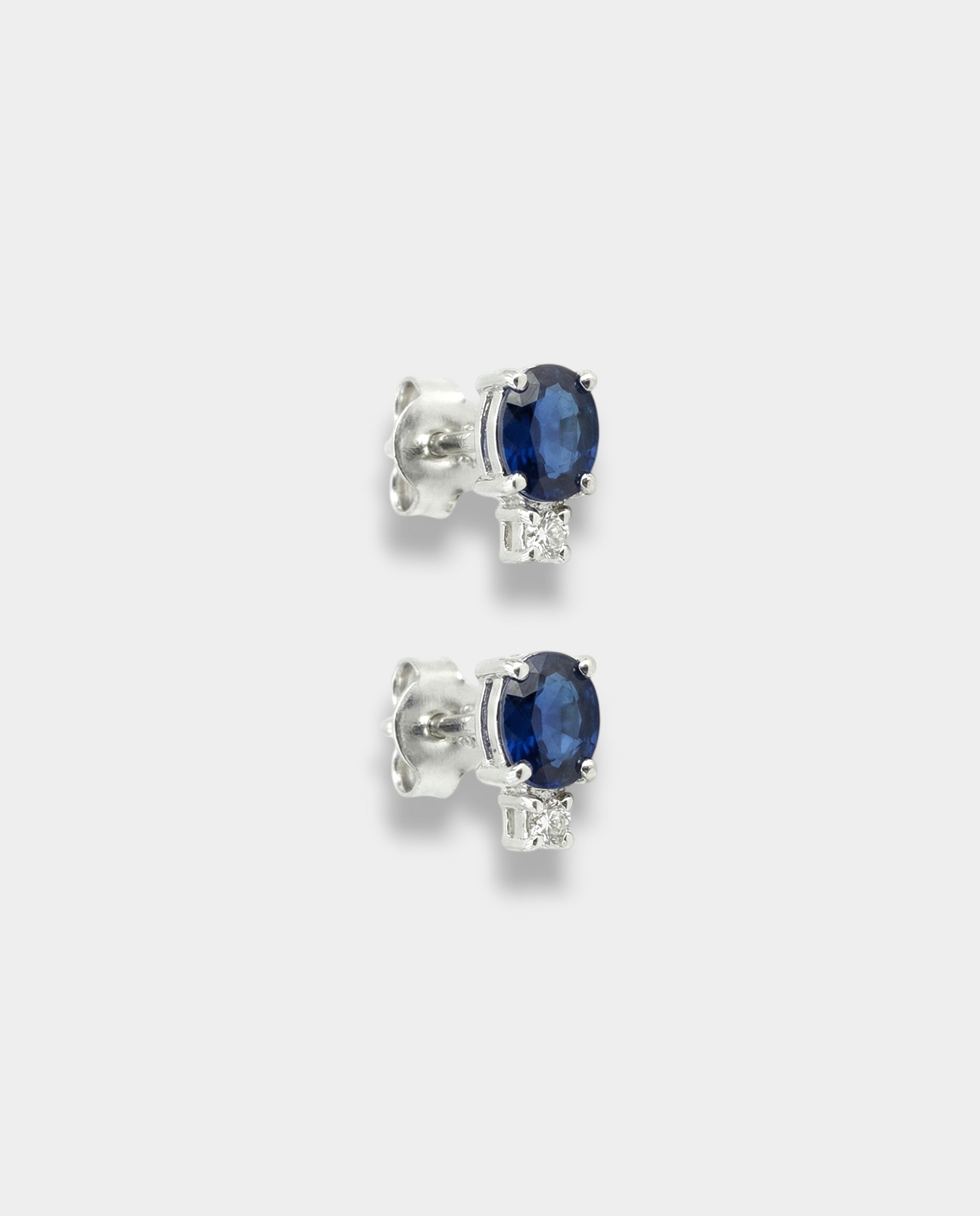 Pair of white-gold earrings with blue sapphires on a light gray background
