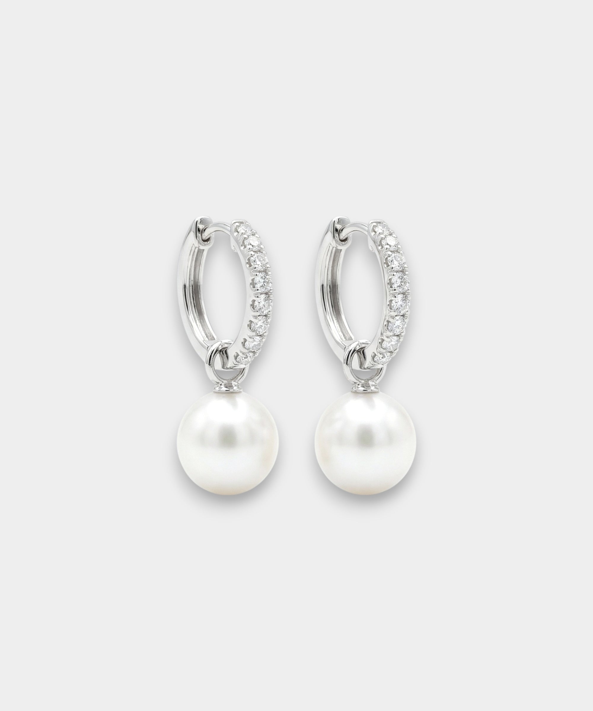 Pair of white gold hoop earrings with pearl drops on a white background