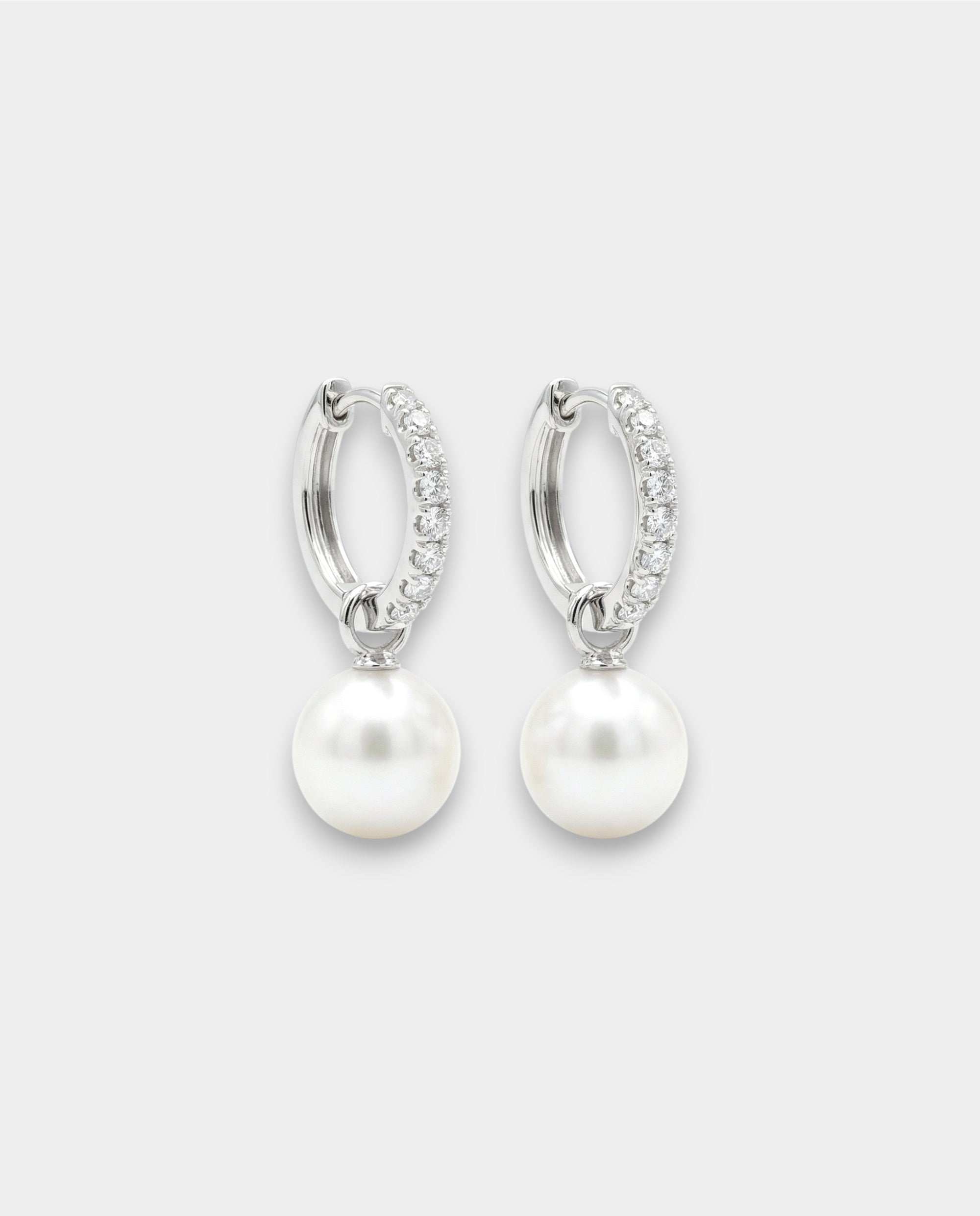 Pair of white gold hoop earrings with pearl drops on a white background