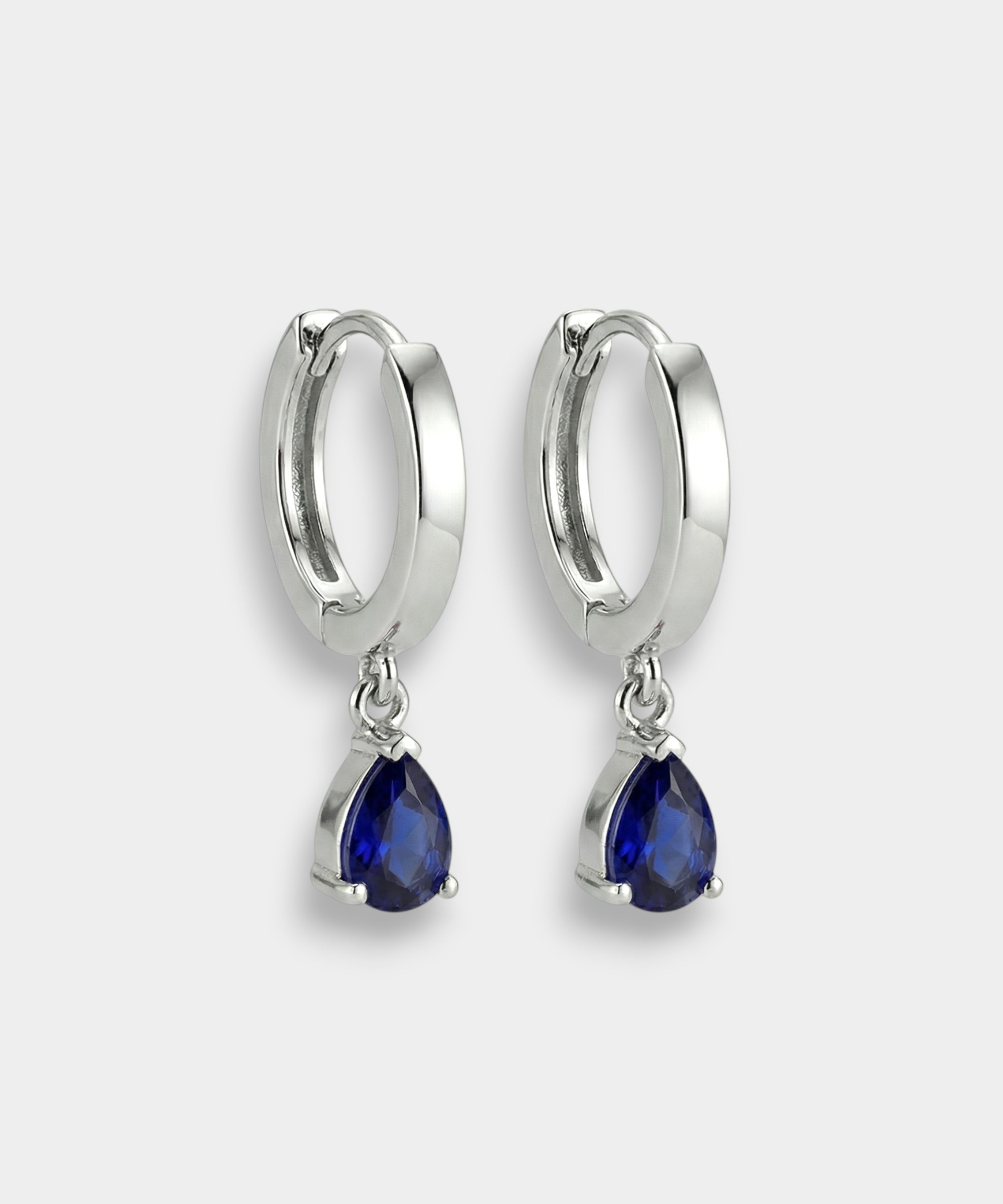 White gold hoop earrings with blue teardrop sapphires on a white background