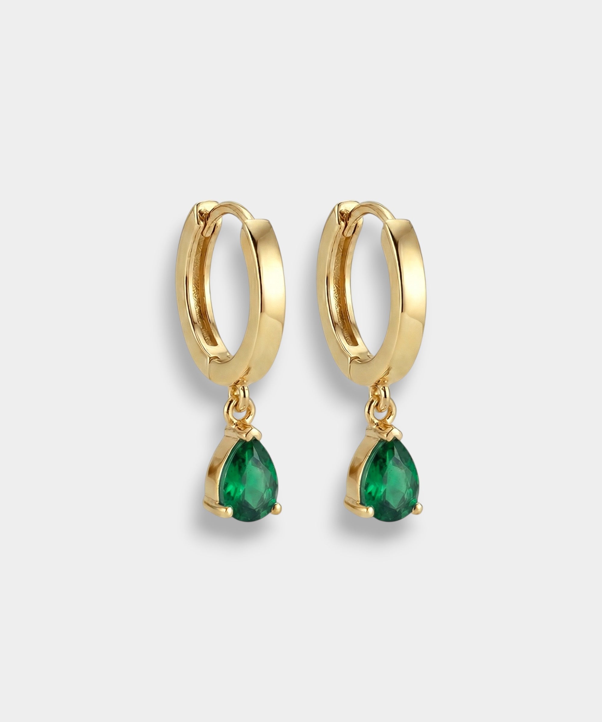 Gold hoop earrings with pear-cut emeralds on a white background
