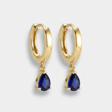 Gold hoop earrings with blue teardrop sapphires on a light gray background
