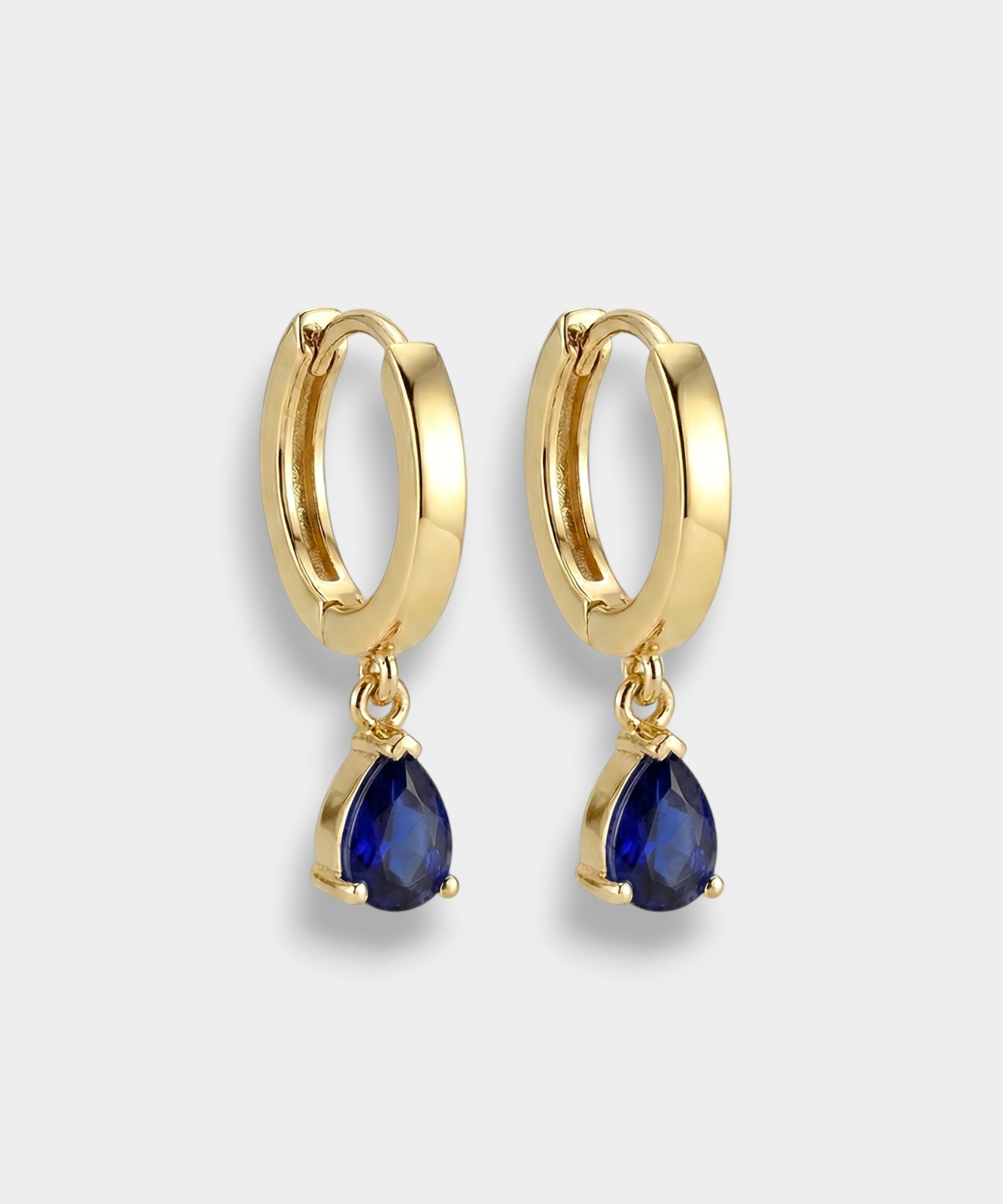 Gold hoop earrings with blue teardrop sapphires on a light gray background